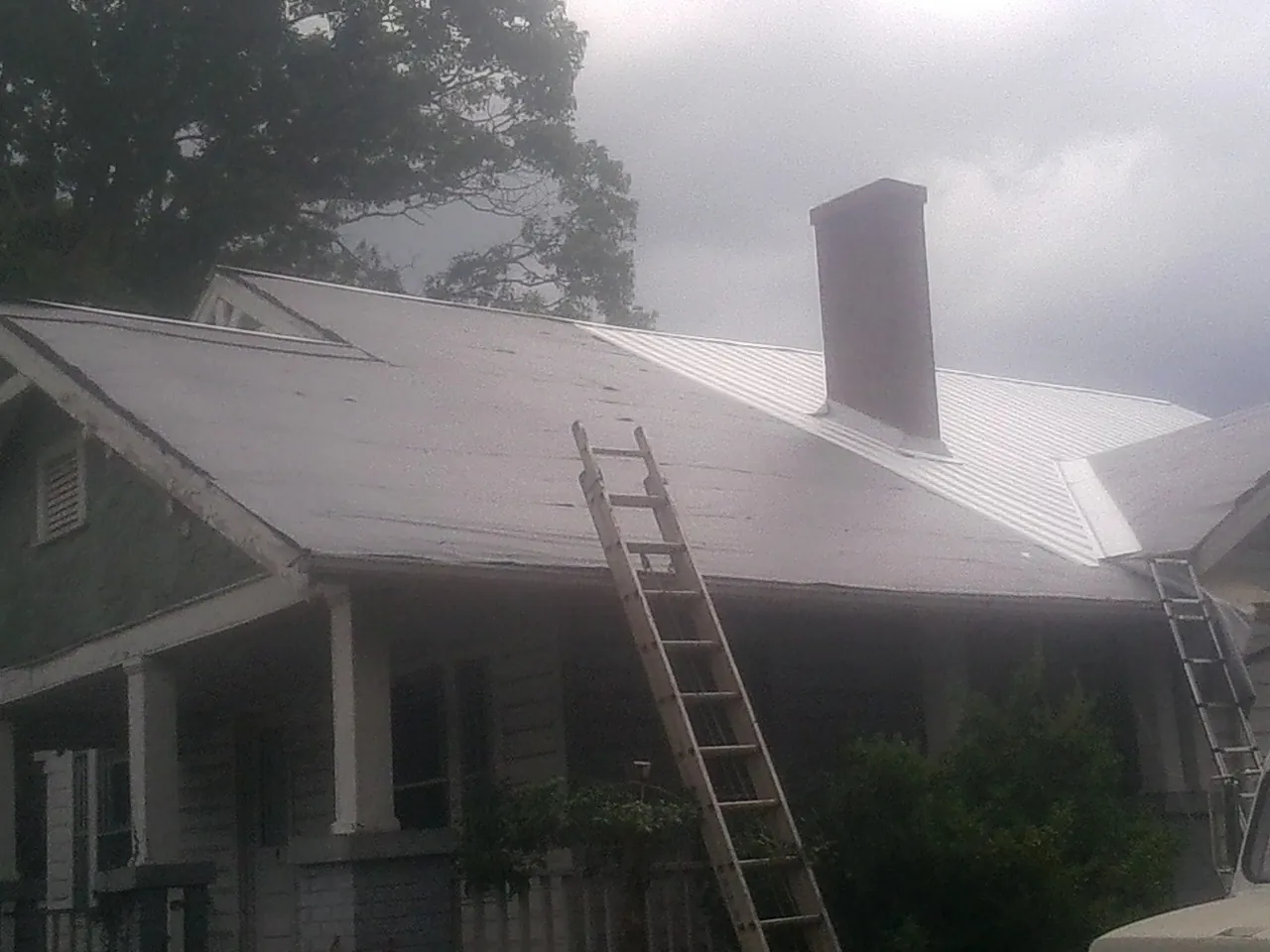 Ladders against a metal roof on an older home with a brick chimney in Jackson