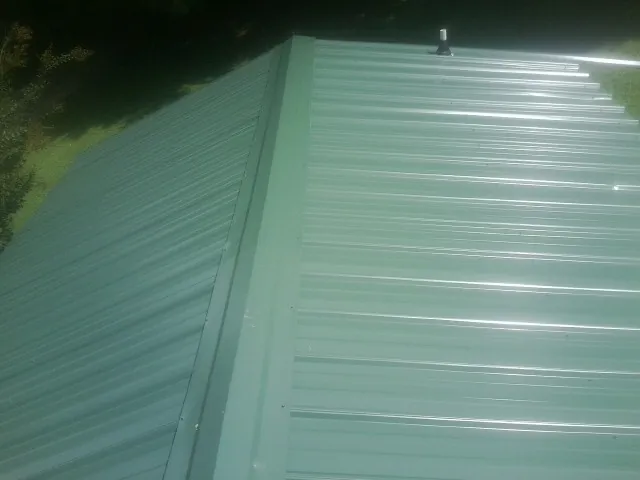 New green metal panels meeting at the ridge of a roof — Flat Roof Repair work by our crew in Jackson